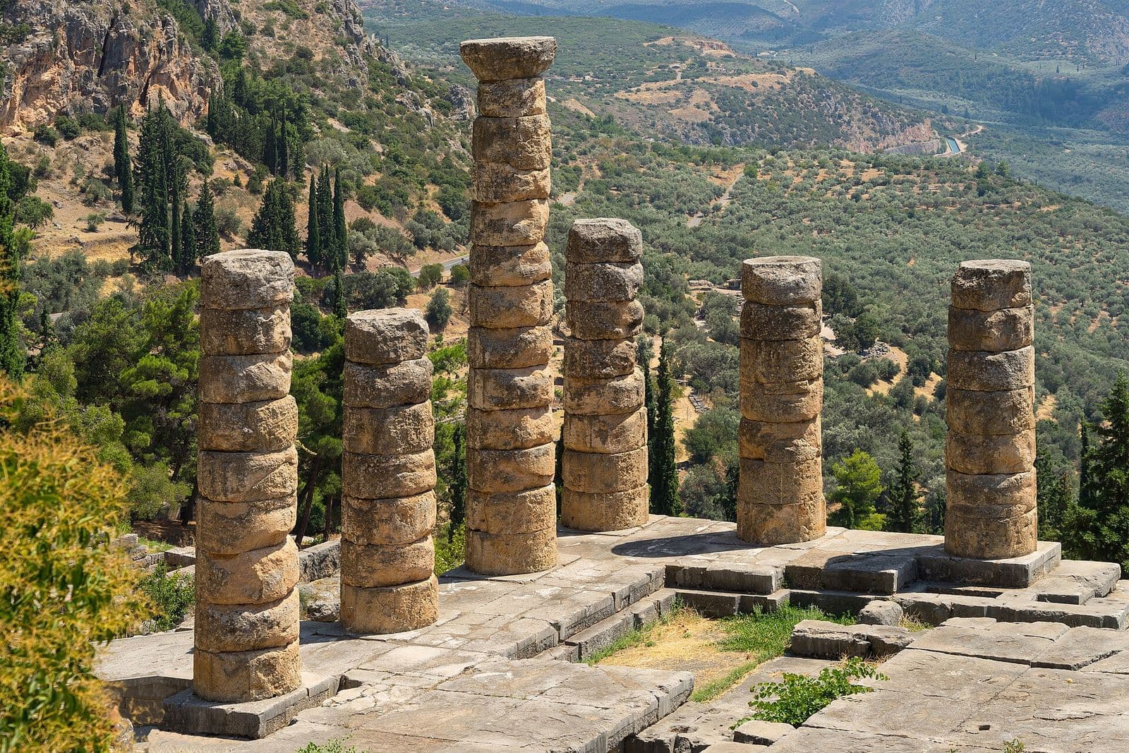 The six standing columns of the temple of Apollo at Delphi, on a slope of olive trees and pines below the mountains