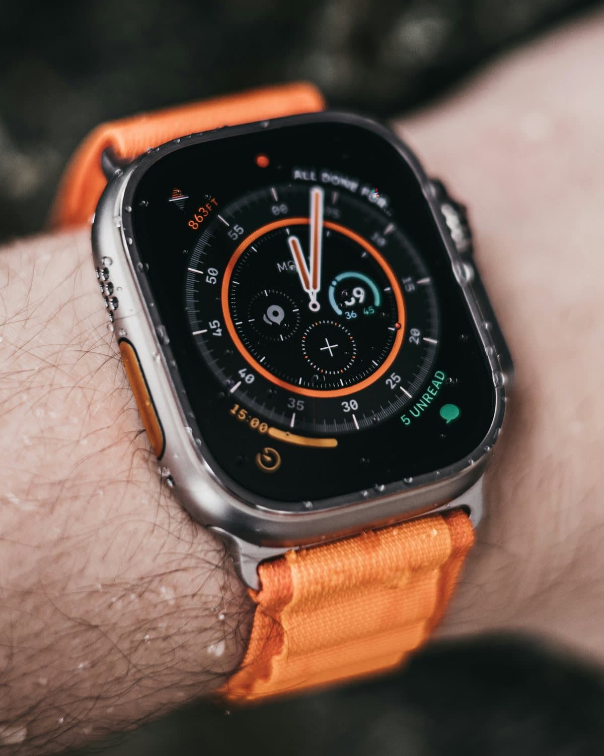 An Apple Watch Ultra on a wet wrist, with an orange loop band and a compass watch face
